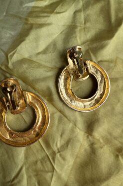Pair of gold-tone hoop earrings with clip-on clasps resting on olive-green fabric