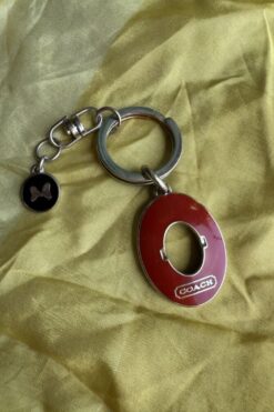 Coach keychain with a red oval tag and butterfly charm on a metal ring, laid on yellow fabric.
