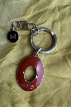 Coach keychain with a red oval tag and metal ring, plus a small black circle charm with a bone motif on fabric backdrop
