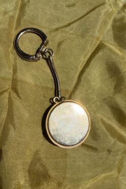 Round metal keychain with a blank circular pendant resting on olive fabric