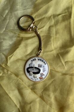 Keychain with a Las Vegas souvenir medallion showing a roulette wheel and playing cards on yellow fabric.