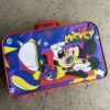 Bright blue Mickey Mouse suitcase with yellow shoes on a concrete surface nearby.