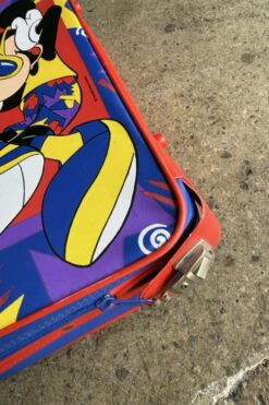 Colorful children's suitcase with a Mickey Mouse graphic on red edges, lying on a concrete surface.