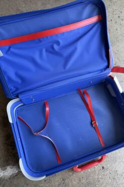Open blue suitcase with red straps inside, resting on a concrete surface.