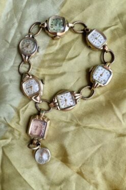 Bracelet made of antique watch faces linked in a circle, with a square pendant showing a portrait and a small round locket against green fabric.