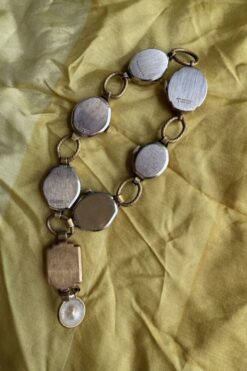 Antique metal watch chain with multiple round watch cases linked together on a yellow fabric background.